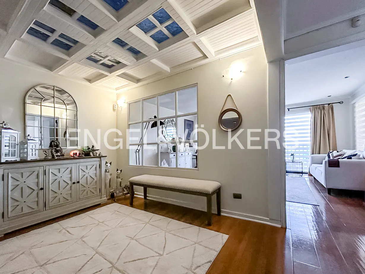 Interior view of a living room with white walls, a patterned ceiling, and hardwood floors. A cabinet, bench, and rug furnish the space.