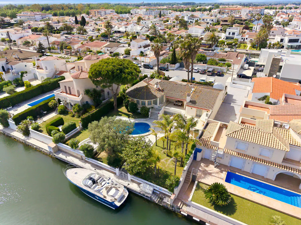 Aerial view of waterfront homes with pools, palm trees, and a boat docked on a canal in a residential neighborhood.
