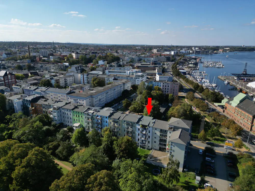 Aerial view of a multi-story apartment building with an arrow pointing to the roof, city and harbor in background.