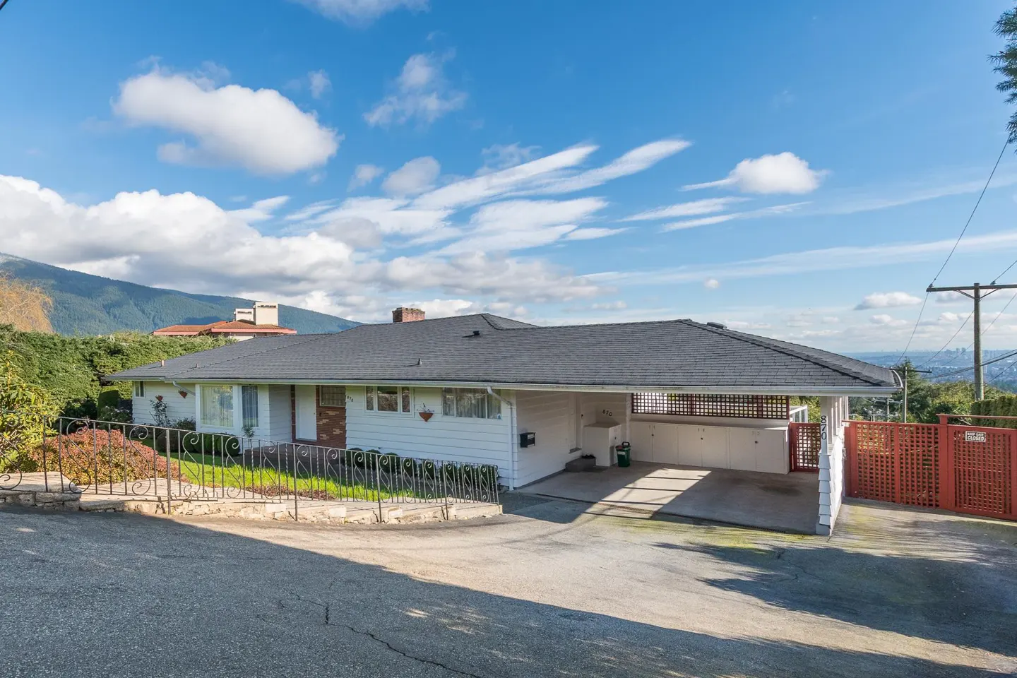 Exterior view of a white single-story house with a dark gray roof and a carport on a sunny day.