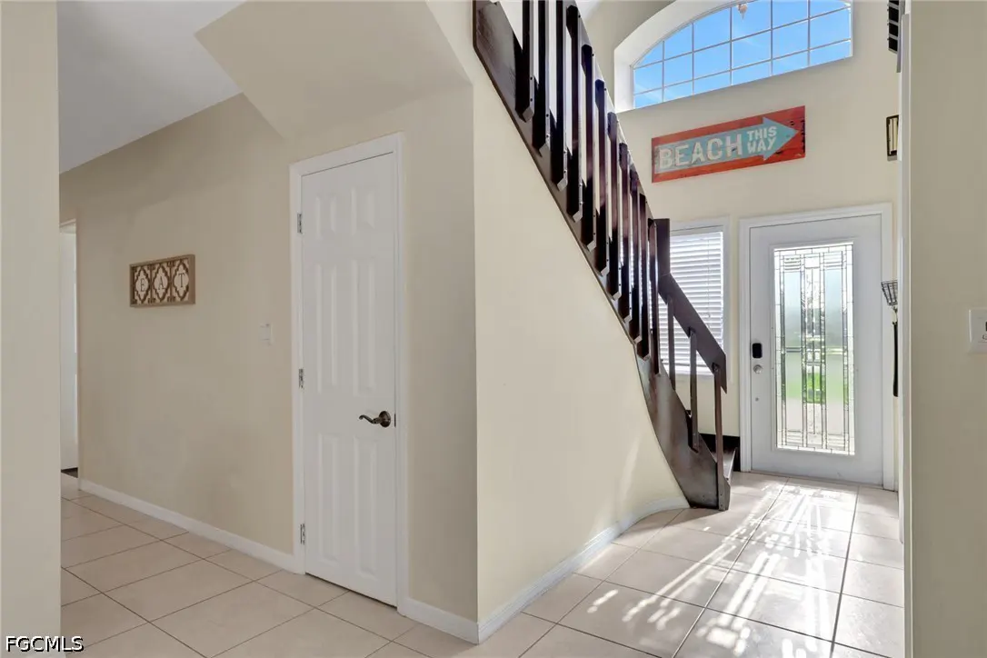 Beige foyer with tile floor, white door, and dark wood staircase. A "Beach This Way" sign hangs above the front door.