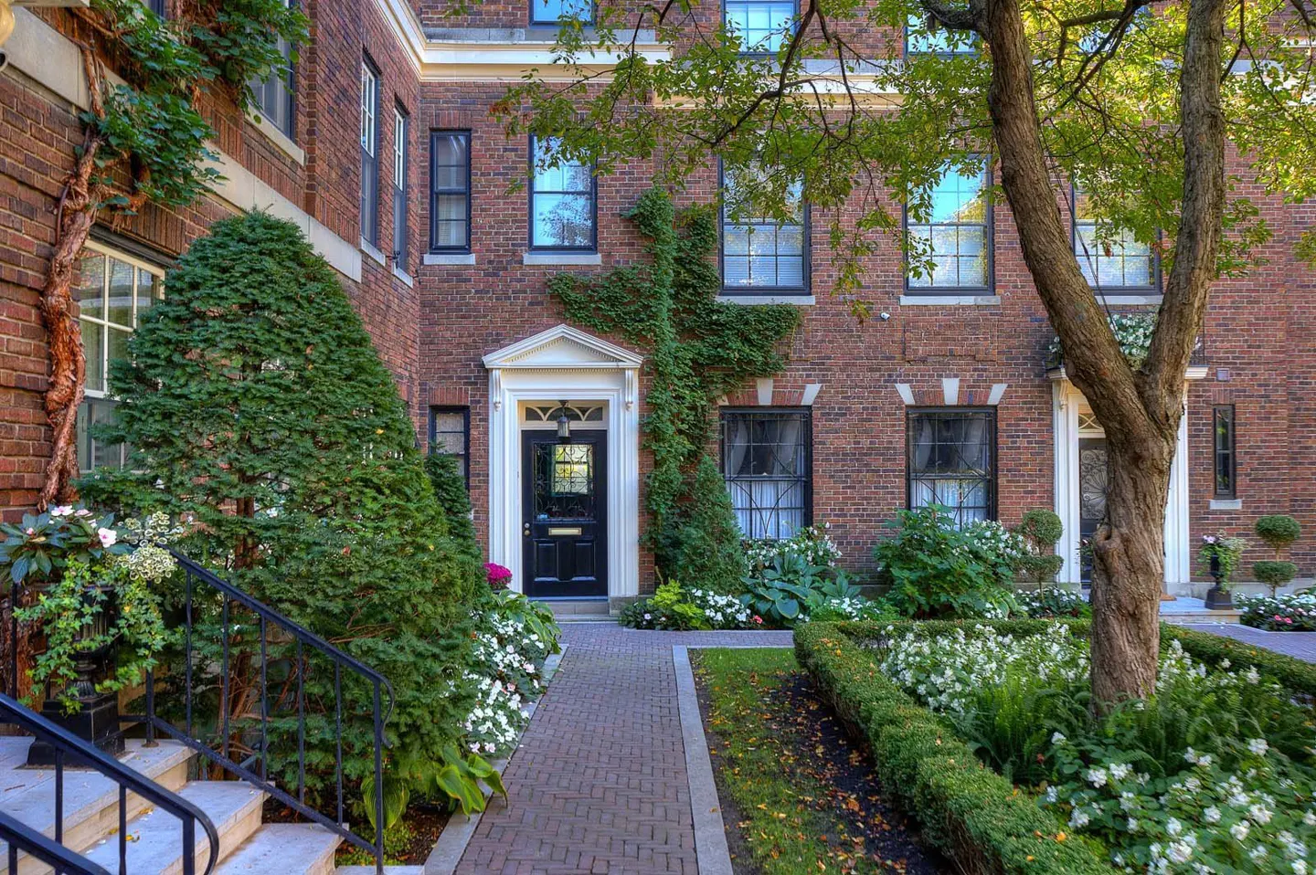 Brick building with black door and white trim, green ivy, and manicured garden with white flowers.
