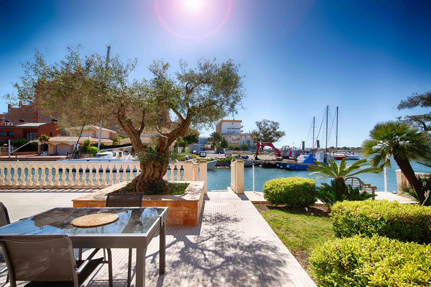 Outdoor patio with a glass table and chairs overlooks a marina with boats and a blue sky.
