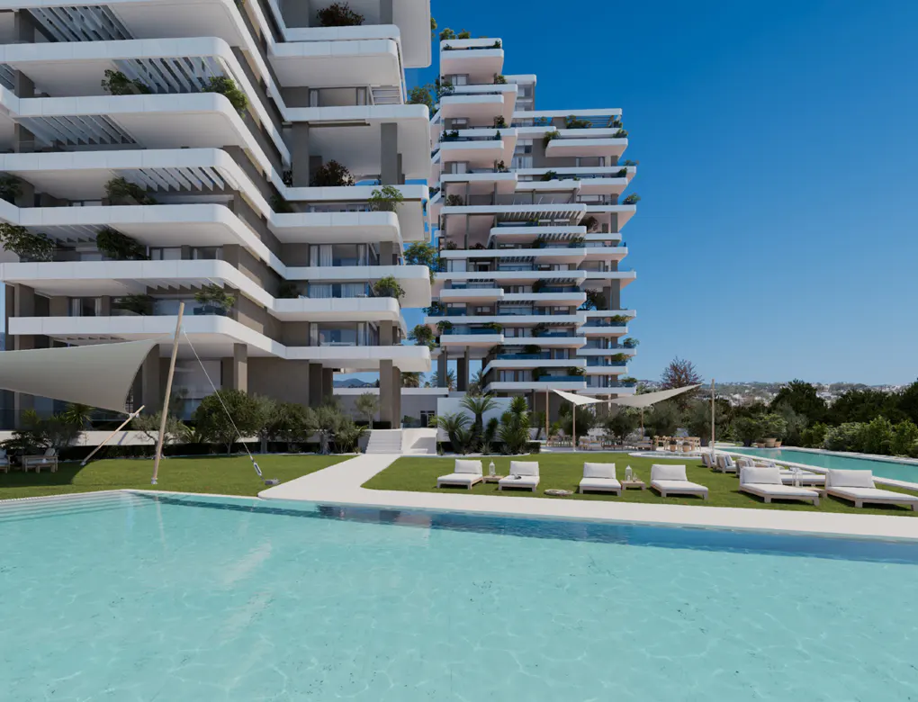 Modern apartment complex with a pool. White lounge chairs sit on the green lawn. Balconies with plants adorn the building.