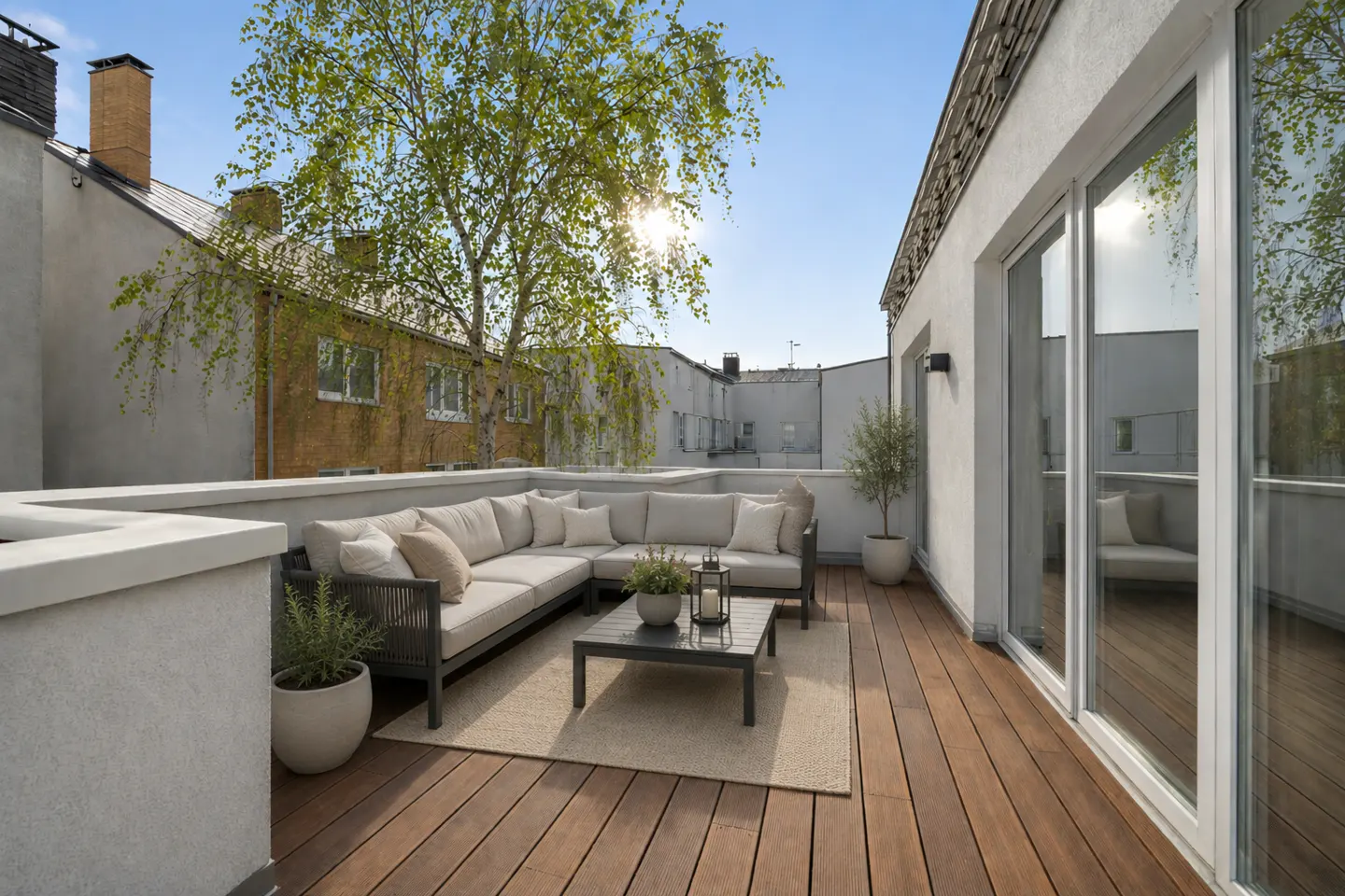 Modern rooftop terrace with a wooden deck, L-shaped sofa, coffee table, and potted plants under a sunny blue sky.