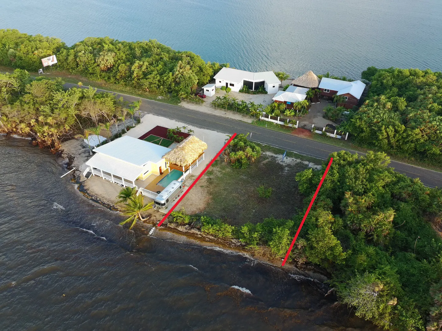 Aerial view of waterfront property with red boundary lines, a yellow house, pool, and an Airstream trailer.