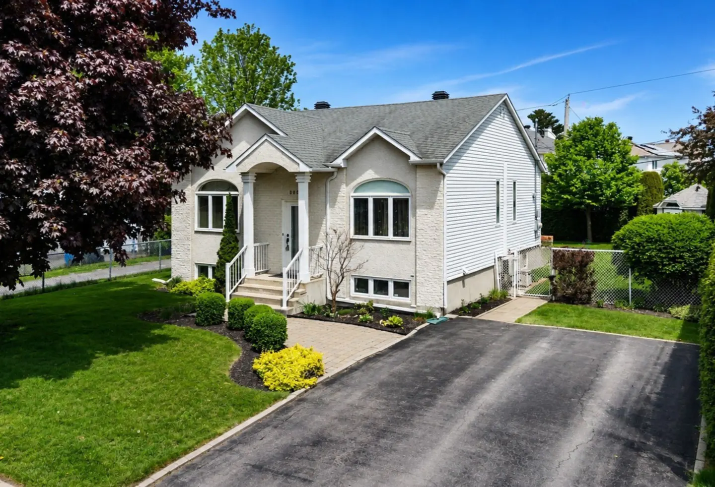 Two-story house with white siding, a gray roof, and a black asphalt driveway on a sunny day.