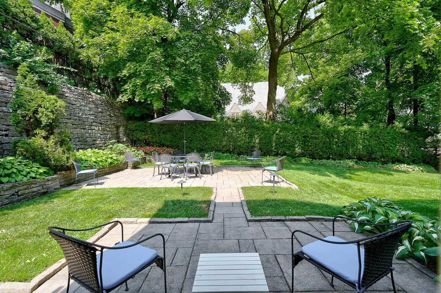 A backyard with a stone patio, green grass, and a table with chairs under an umbrella.