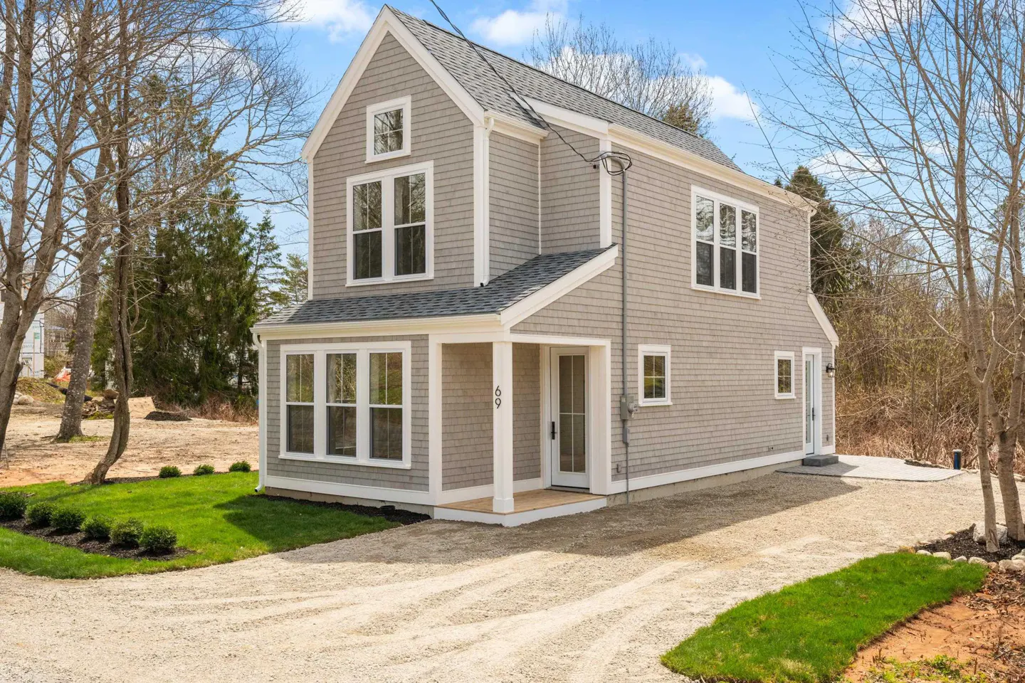 Two-story gray house with white trim, a gravel driveway, and green grass. The house has a covered porch and many windows.
