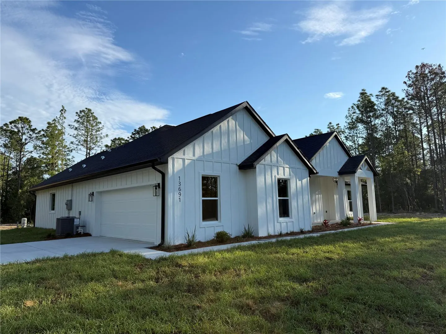 Modern white farmhouse with black roof and trim, featuring a two-car garage and grassy yard under a blue sky.