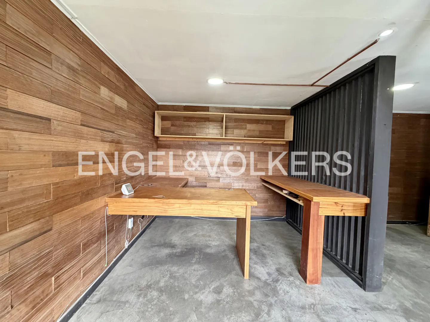 Modern home office with wood-paneled walls, two wooden desks, floating shelves, and a black slatted room divider.