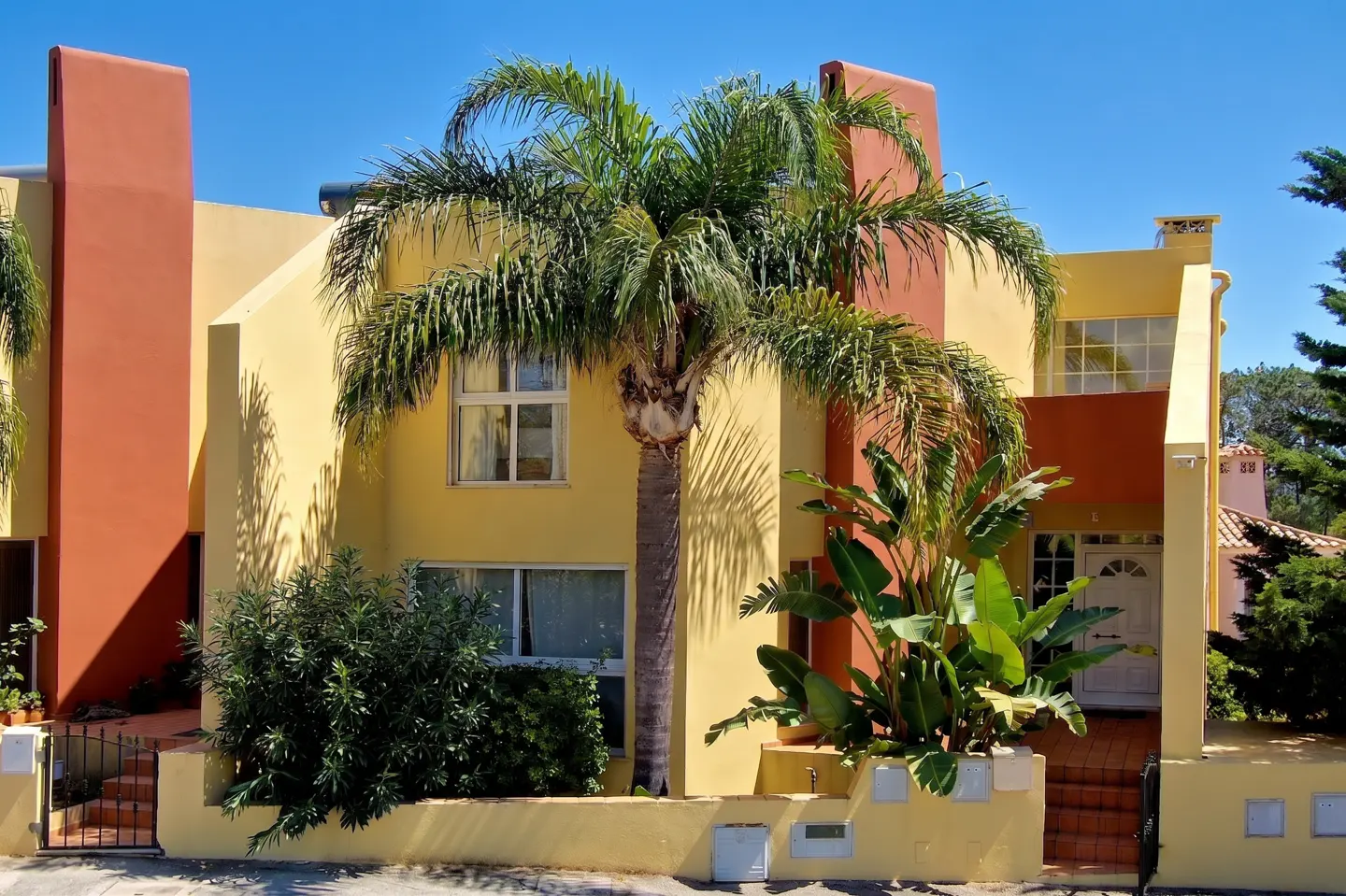 Exterior of a yellow and orange townhouse with a palm tree in front, under a clear blue sky.