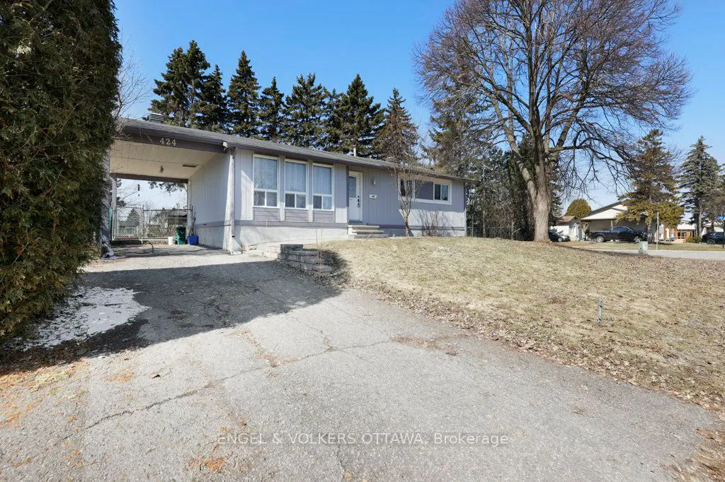 Exterior view of a one-story, light gray house with a carport and a cracked driveway on a sunny day.