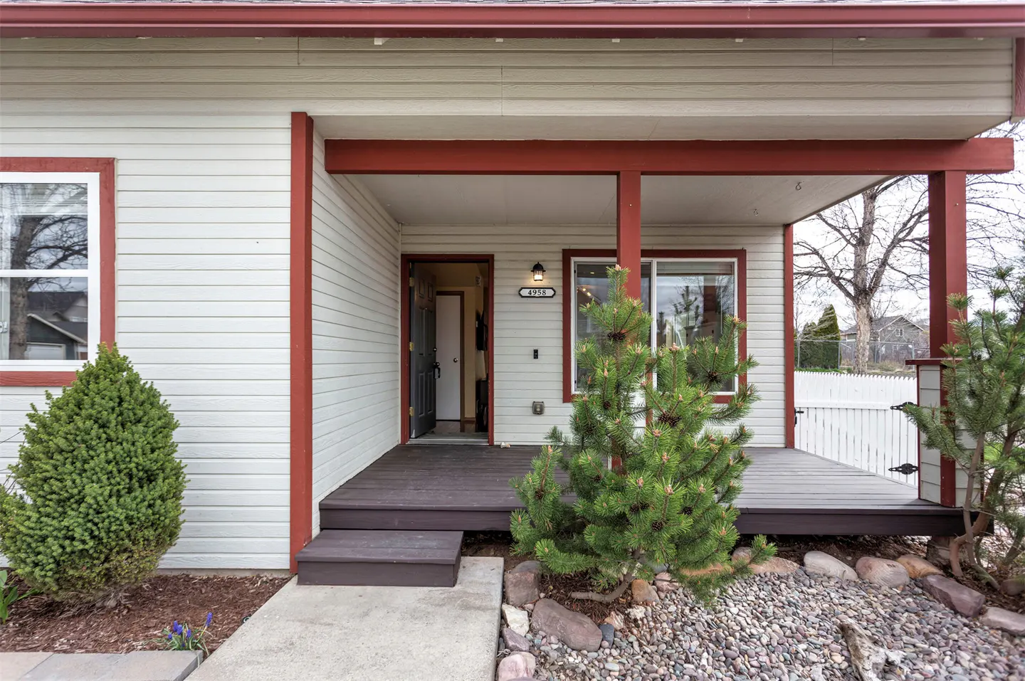 Front exterior of a house with beige siding, red trim, and a dark wood porch. The front door is open.