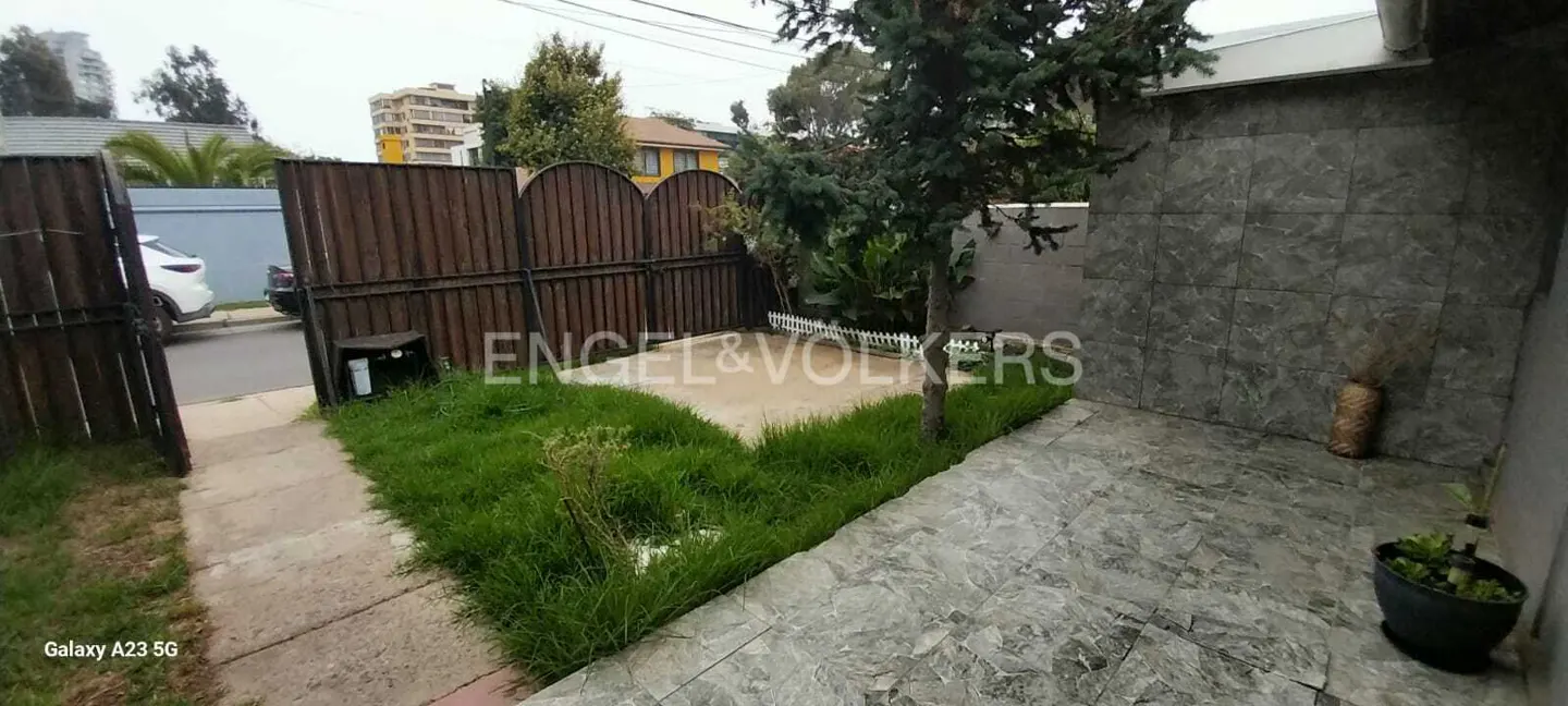 A view of a home's front yard with a brown fence, green grass, and a gray stone wall.