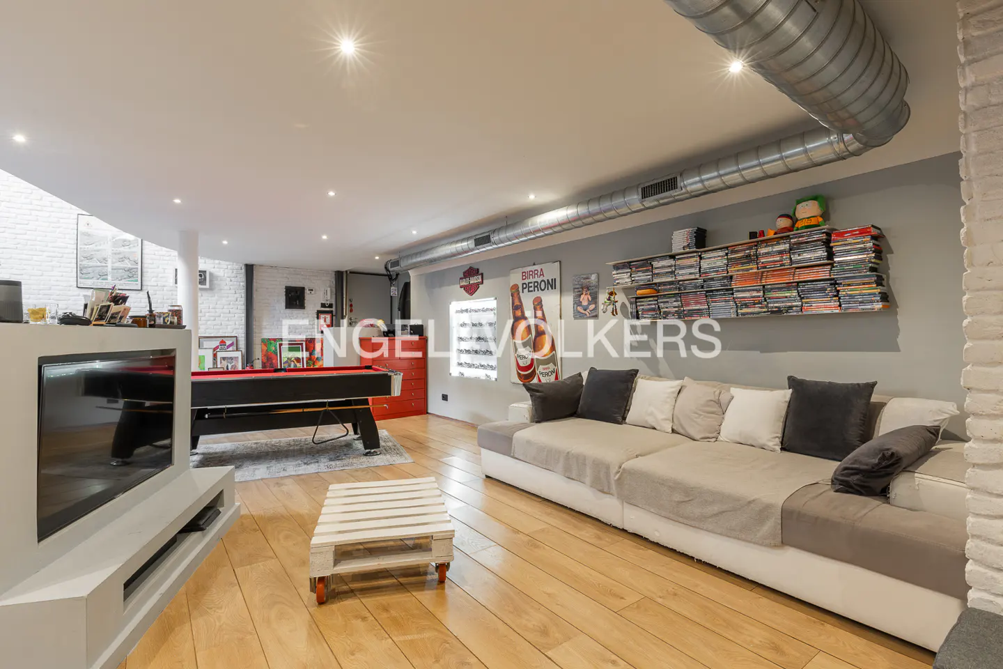 Living room with a pool table, a large sofa, and a TV. The room has wooden floors and white brick walls.