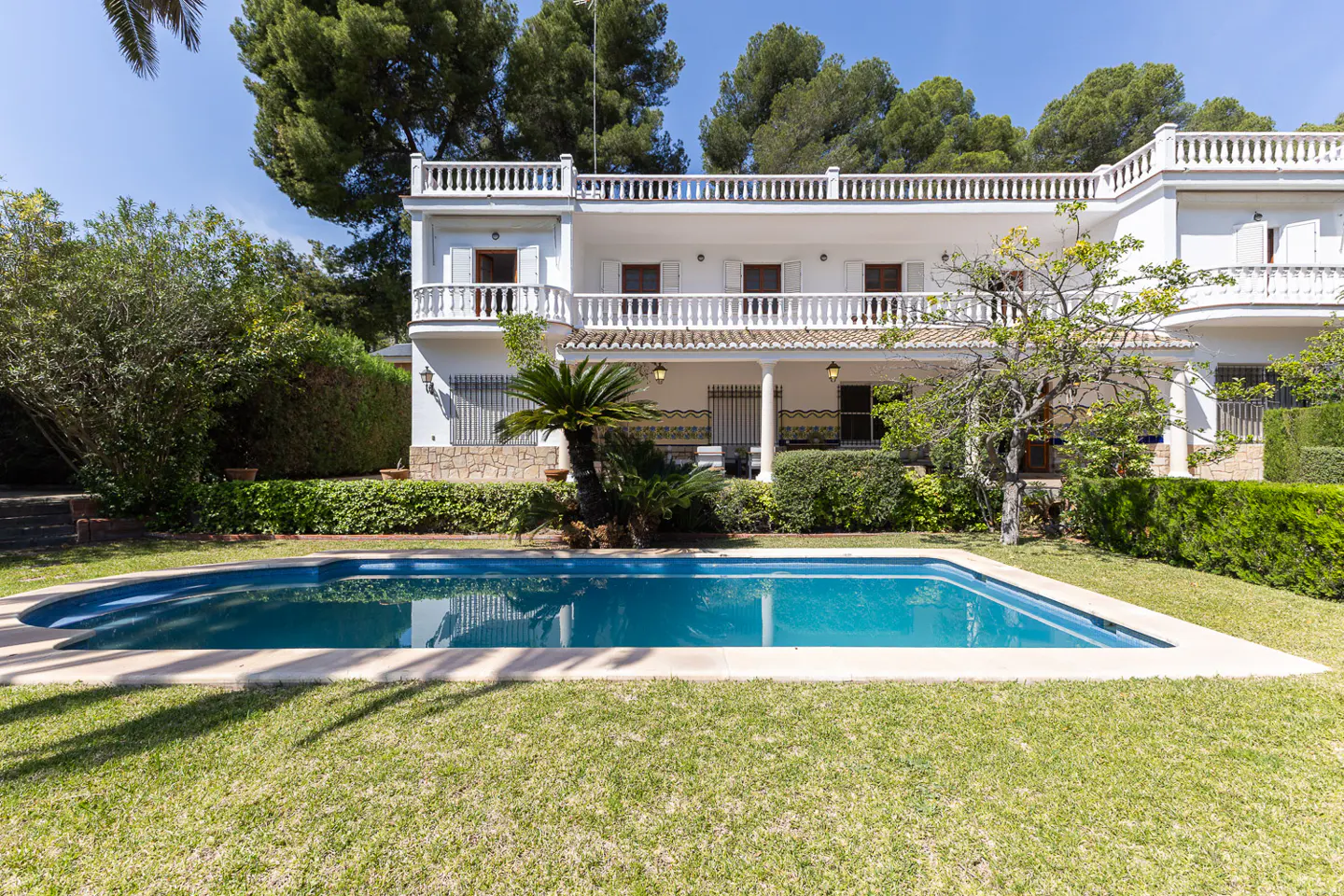 Exterior of a white two-story house with a blue swimming pool and green lawn.