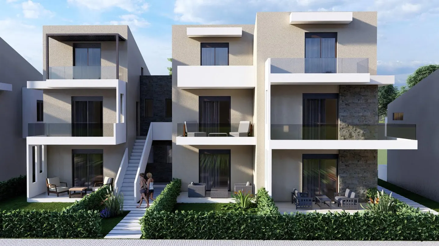 Three-story modern townhouses with balconies and stone accents, surrounded by green hedges and a walkway. Two women walk on the path.