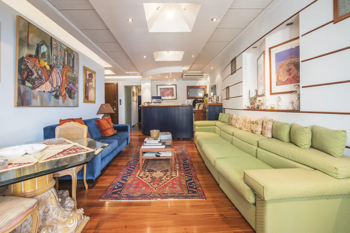 A living room with a blue sofa, a green sofa, a wooden floor, and a colorful rug. There is a painting on the wall.