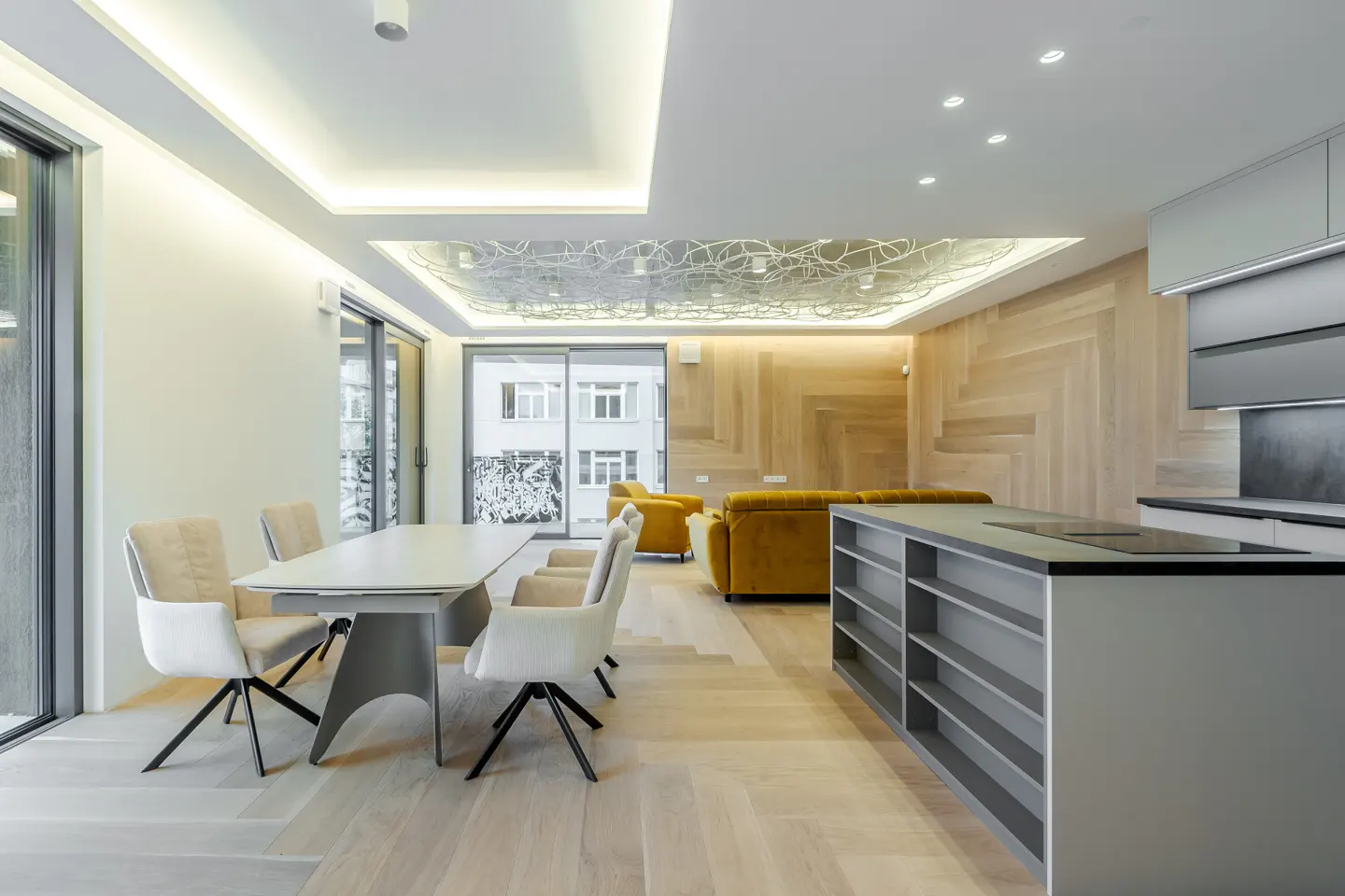 Open-concept living space with a dining table, kitchen island, and mustard-colored sofa. Wood floors and accent wall. Modern lighting.