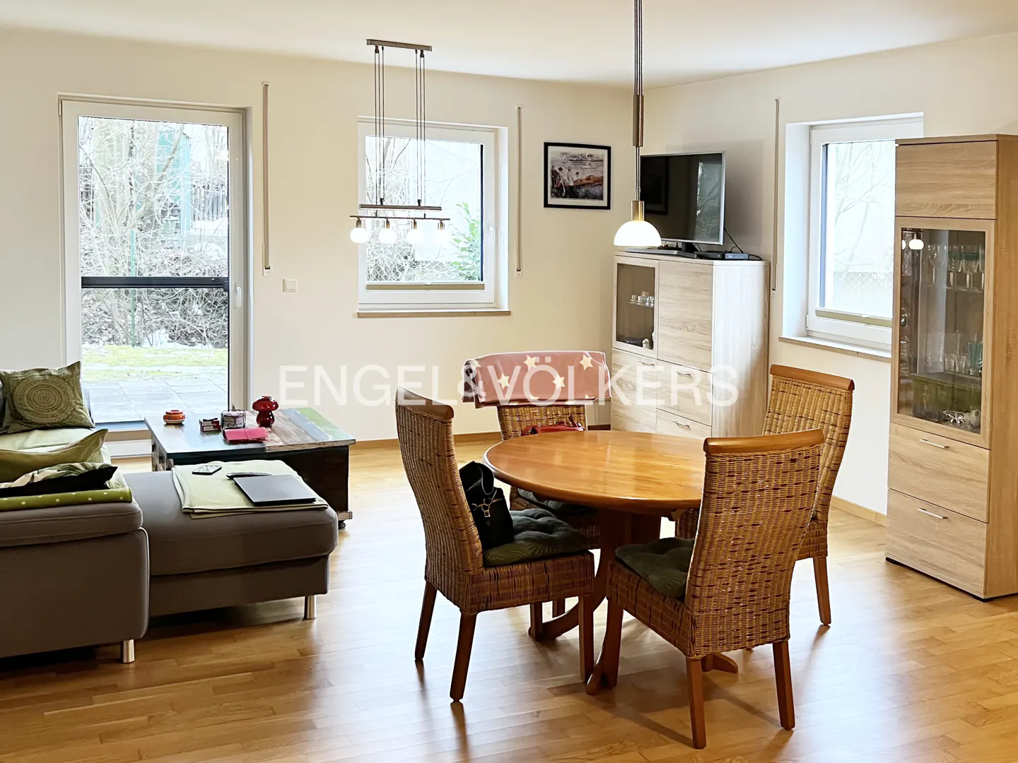 Living room with wood floors, a gray sofa, a round wood table with wicker chairs, and light wood cabinets.