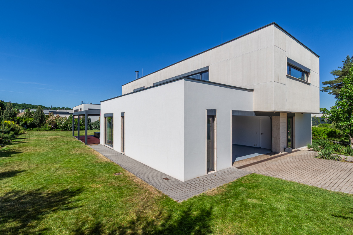 Modern two-story white house with a green lawn and blue sky. A paved walkway leads to the house.
