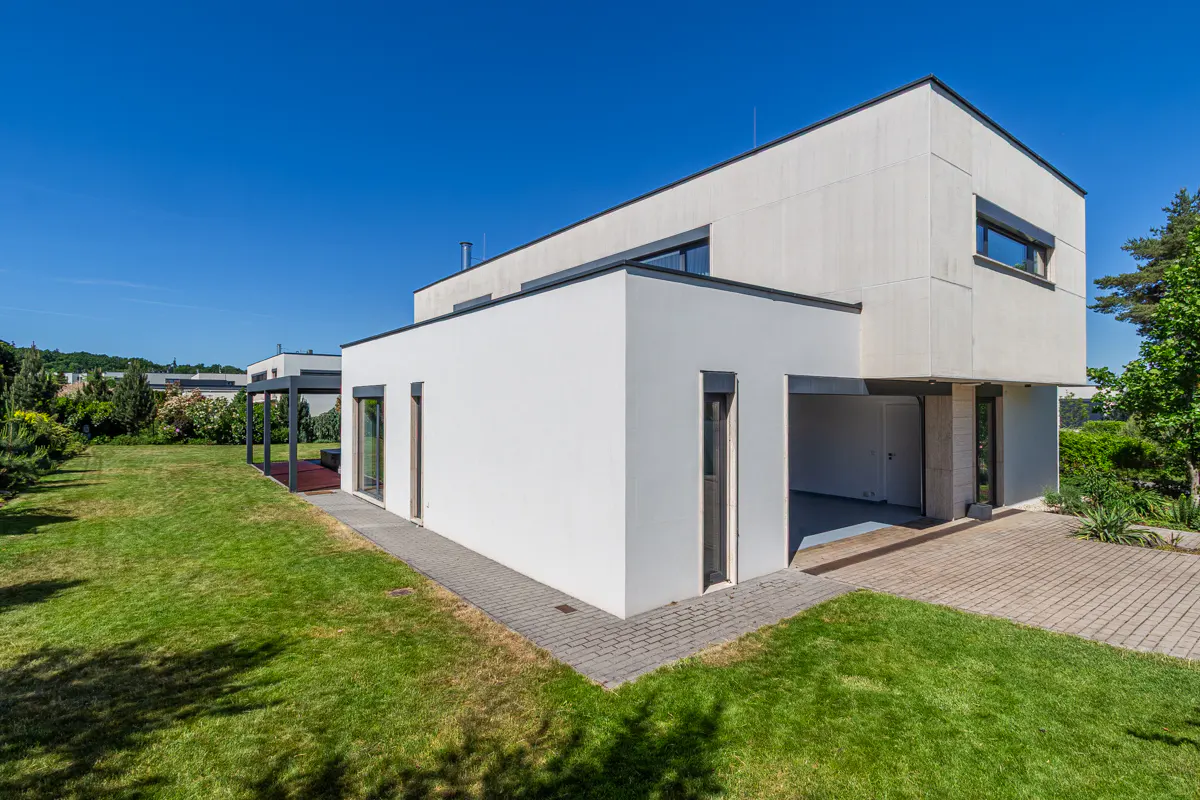 Modern two-story white house with a green lawn and blue sky. A paved walkway leads to the house.