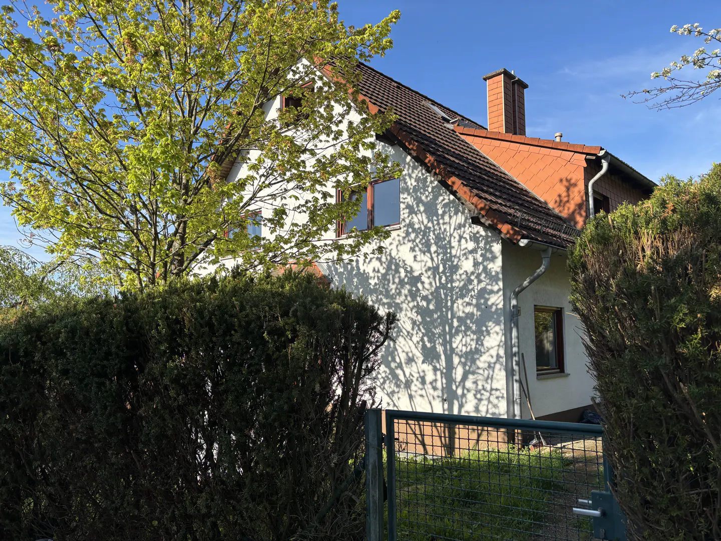 A two-story white house with a red tile roof, chimney, and green trees in the yard.