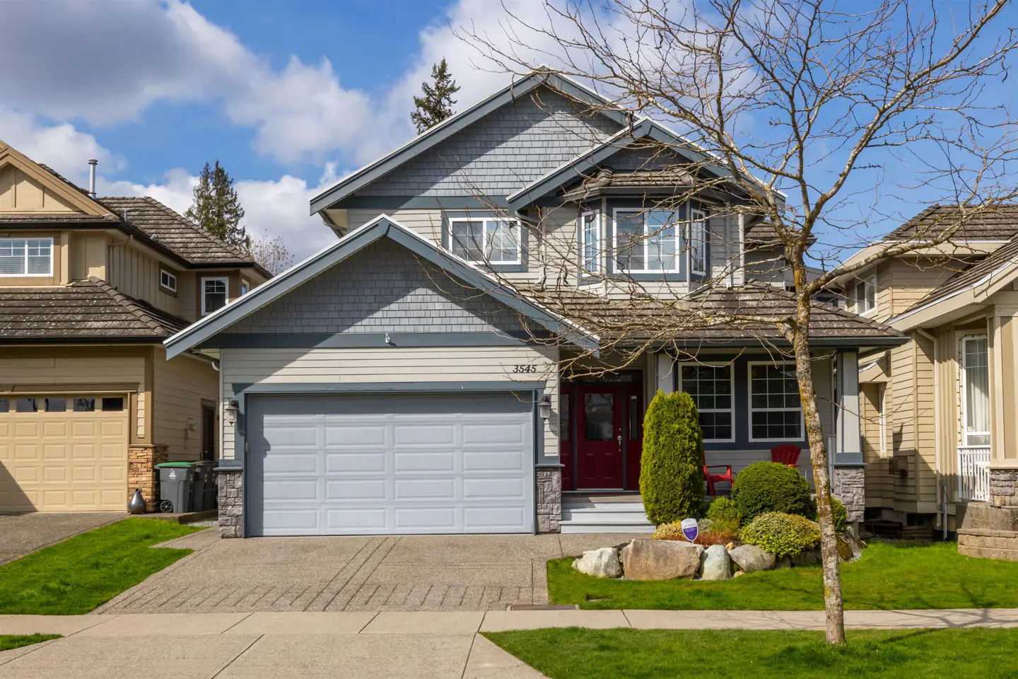 Two-story house with gray shingles, beige siding, white trim, and a gray garage door on a sunny day.