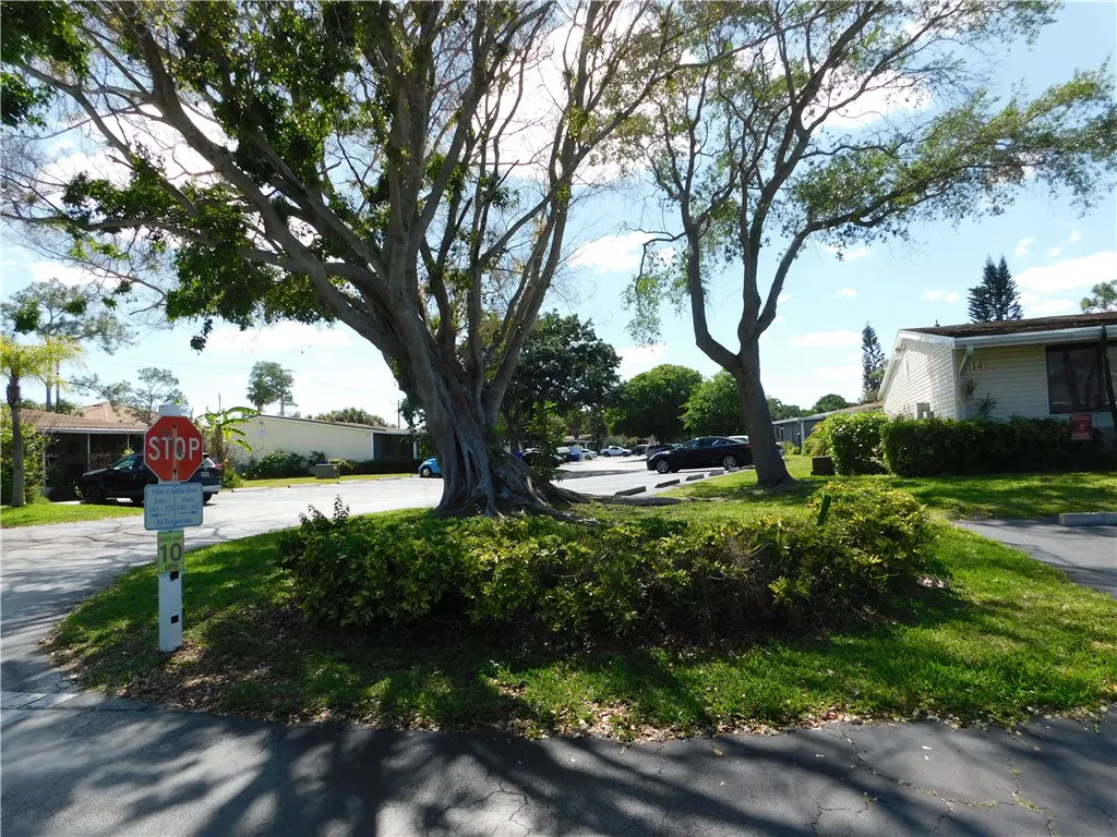 A street view of a residential area with trees, grass, and parked cars. A stop sign is visible on the left.