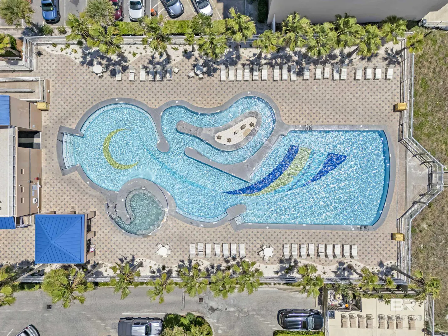Aerial view of a blue swimming pool with lounge chairs and palm trees surrounding it.