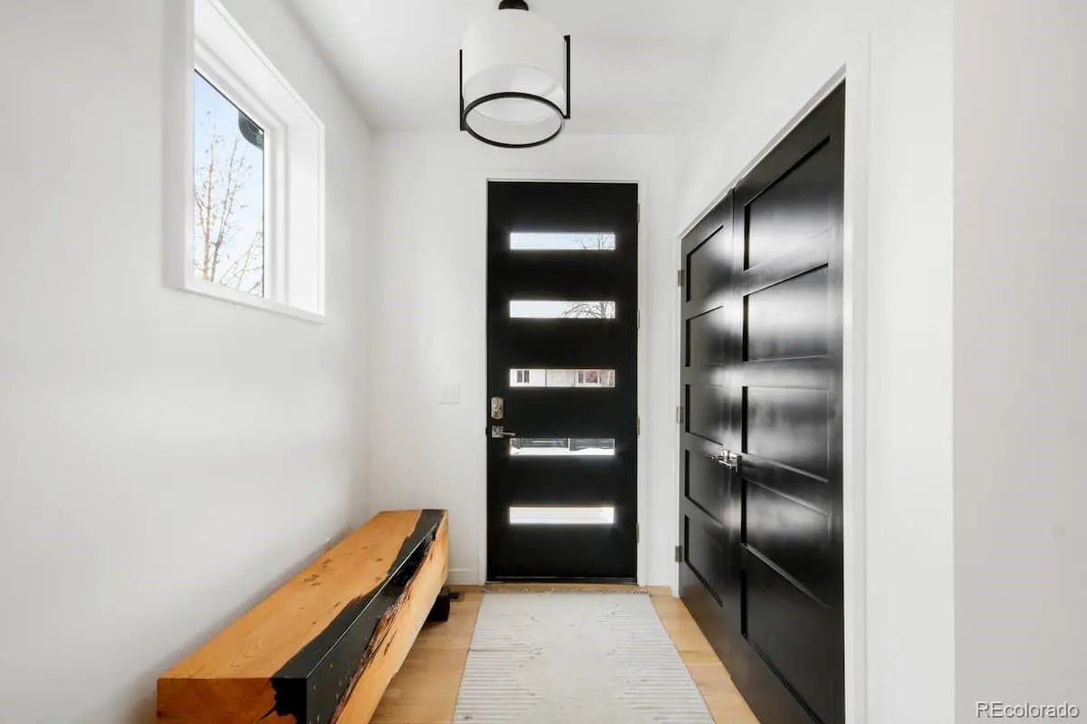 Entryway with white walls, wood floors, and a black front door with horizontal windows. A wooden bench sits to the left.