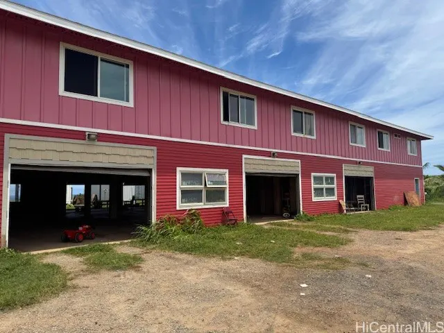 Two-story red barn-style building with multiple garage doors and windows under a blue sky.