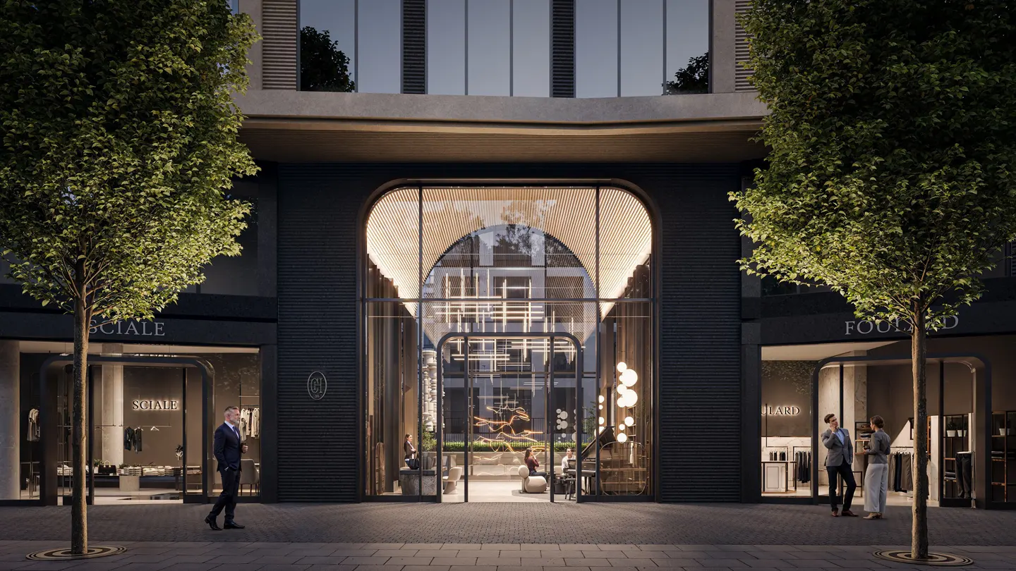 Building exterior with a large arched entrance, flanked by retail spaces and trees. People are visible inside and outside the building.