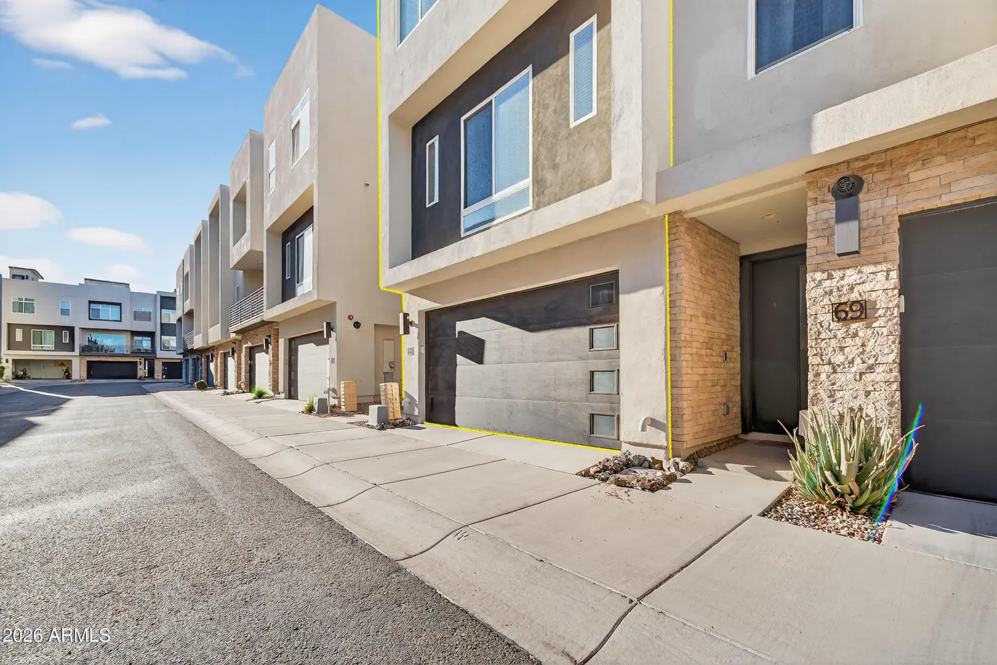 Exterior view of modern townhouses with gray stucco, dark garage doors, and brick accents under a blue sky.