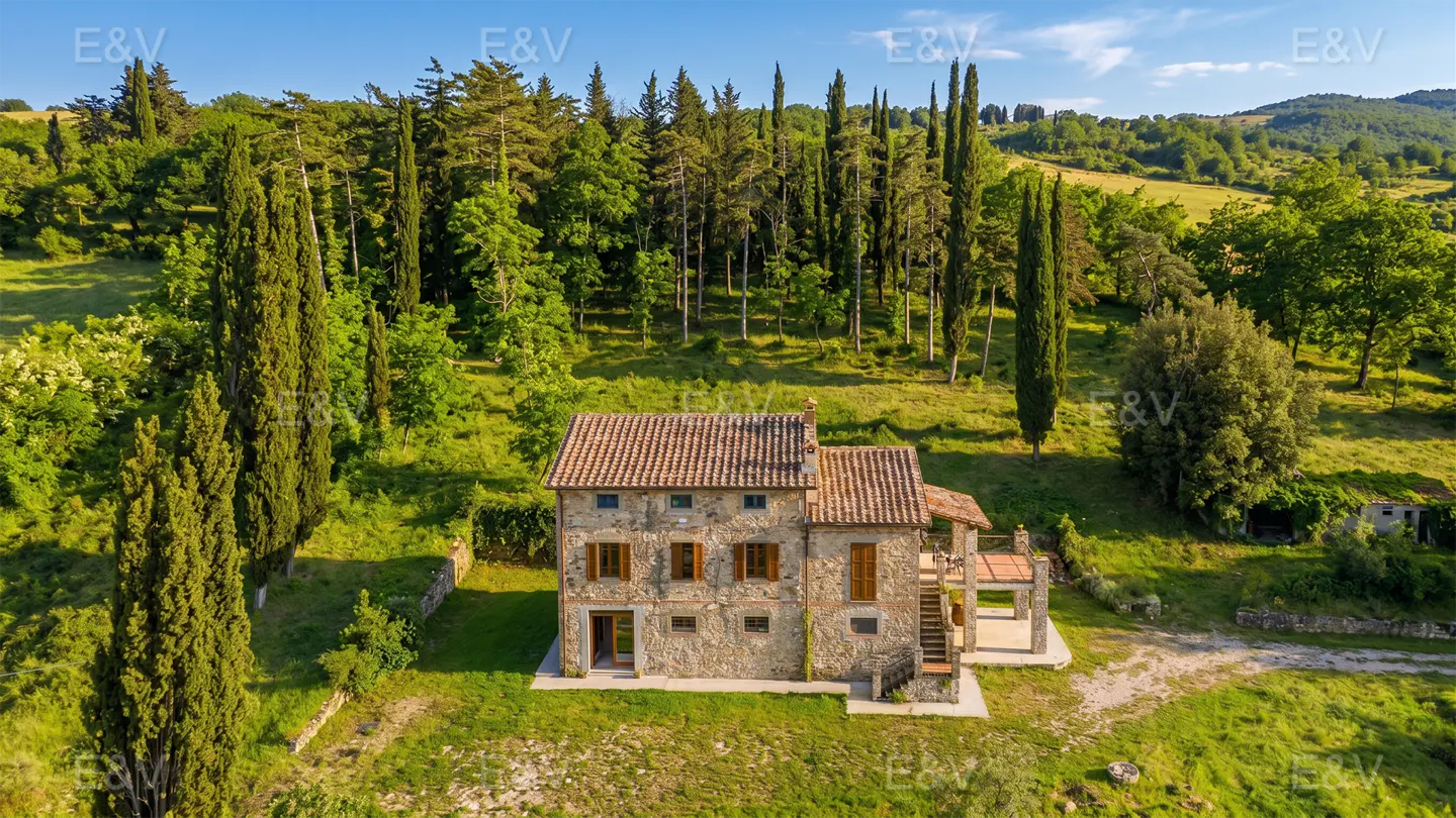 Stone house with a red tile roof, surrounded by green trees and grass.