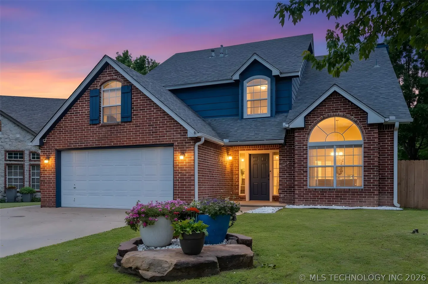 Two-story brick house with blue accents, a white garage door, and flower pots in the front yard.