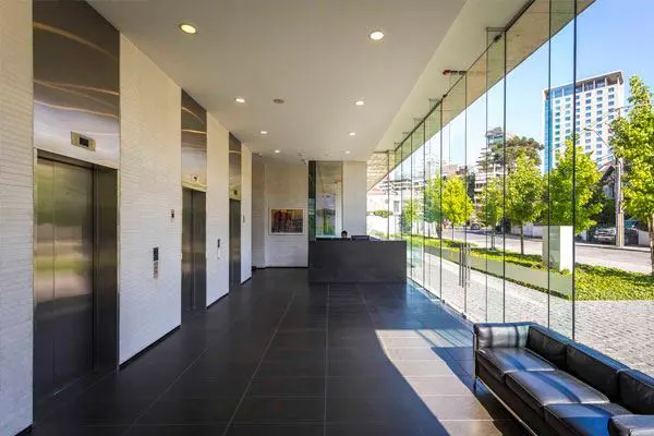Modern building lobby with black tile floor, stainless steel elevators, and a glass wall overlooking trees and a city street.
