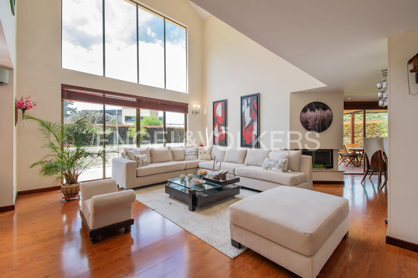 Bright living room with hardwood floors, a large sectional sofa, and floor-to-ceiling windows. Artwork adorns the walls.
