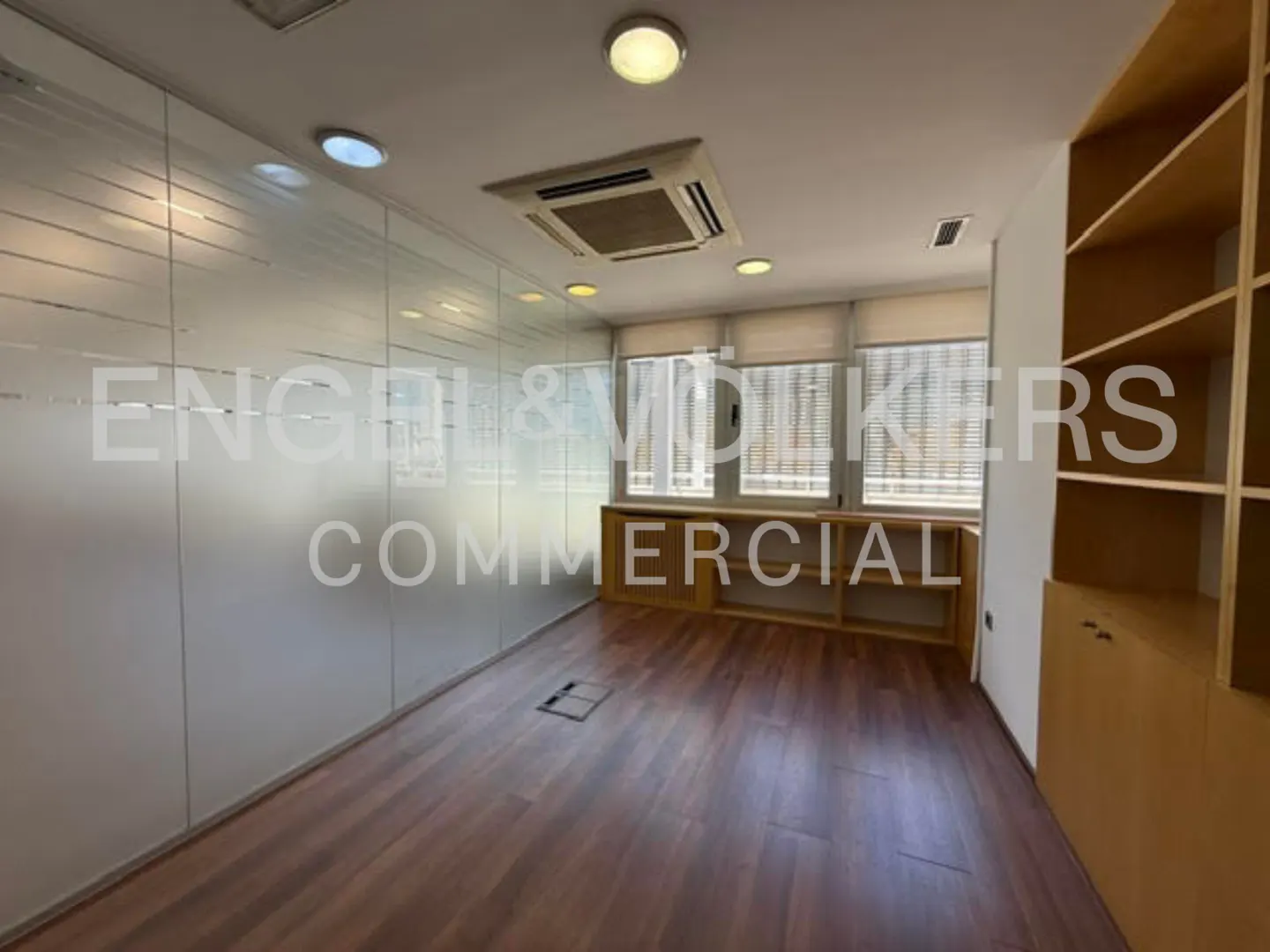 Modern office with wood flooring, a frosted glass wall, built-in wooden shelving, and windows with blinds.