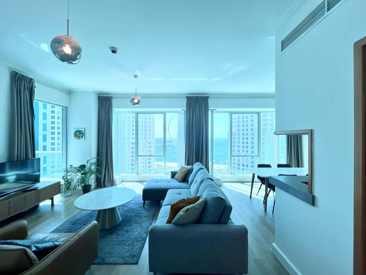 Bright living room with blue sectional sofa, round marble table, and floor-to-ceiling windows with city and ocean views.