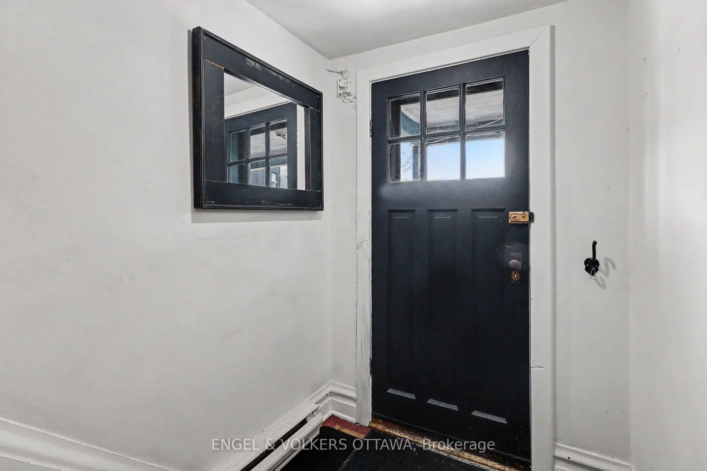 Entryway with a black front door with glass panes, a black framed mirror on the white wall, and a coat hook.
