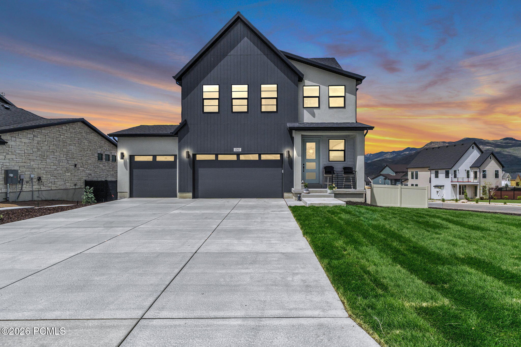 Two-story house with gray siding, a concrete driveway, and a green lawn. The sky is a mix of orange, pink, and blue.