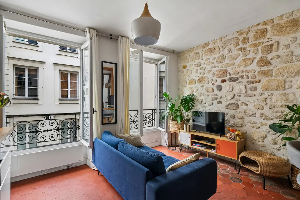 Living room with a blue sofa, TV on a mid-century cabinet, and a rustic stone wall, overlooking a city street.
