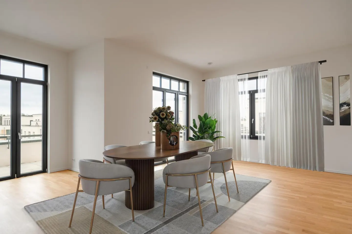 Bright dining room with wood floors, a brown oval table, and six gray chairs with gold legs on a patterned rug. Black framed windows and white curtains.