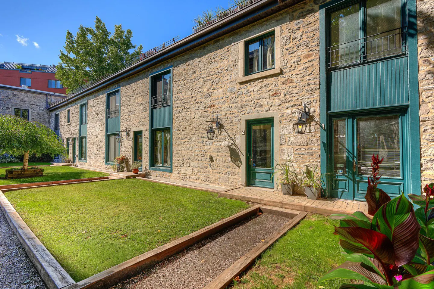 Exterior of a stone building with green trim, a lawn, and a gravel path on a sunny day.