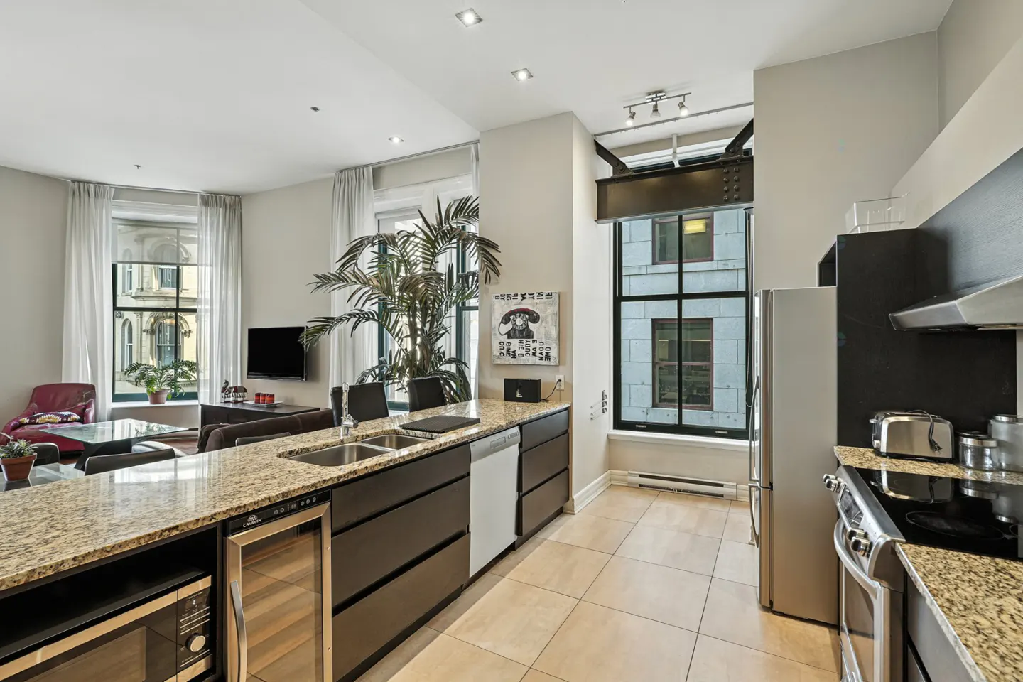 A modern condo kitchen with granite countertops, stainless steel appliances, and a view of a city building.