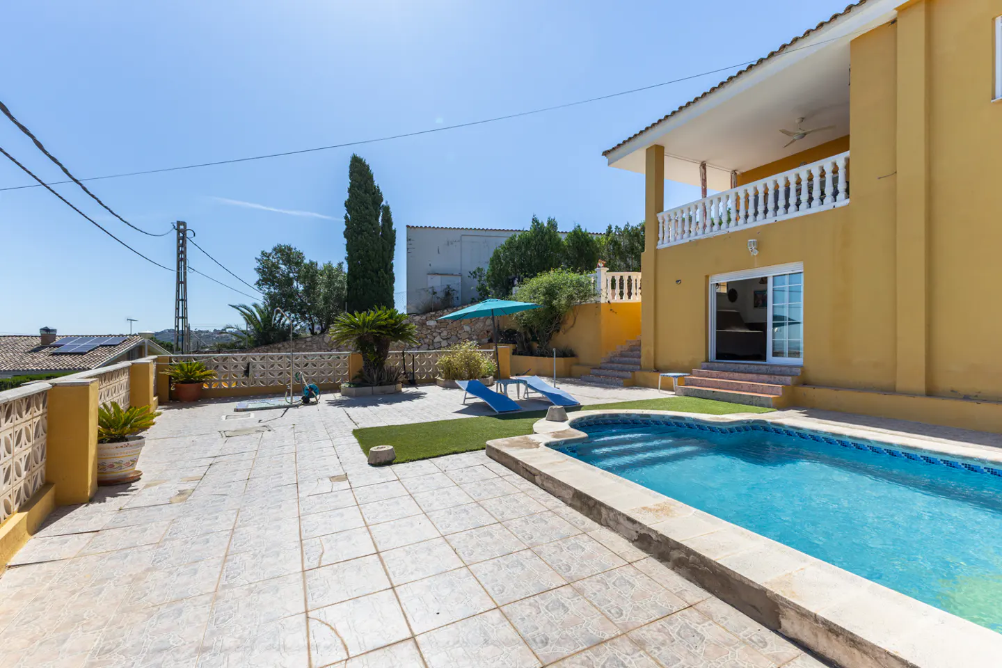 Exterior view of a yellow two-story house with a pool, patio, and blue lounge chairs.