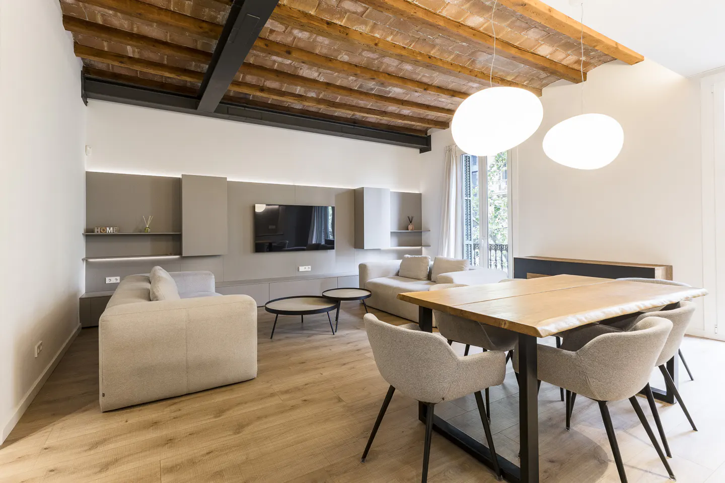 A modern living room with a wood dining table, gray chairs, sofas, and a brick ceiling.