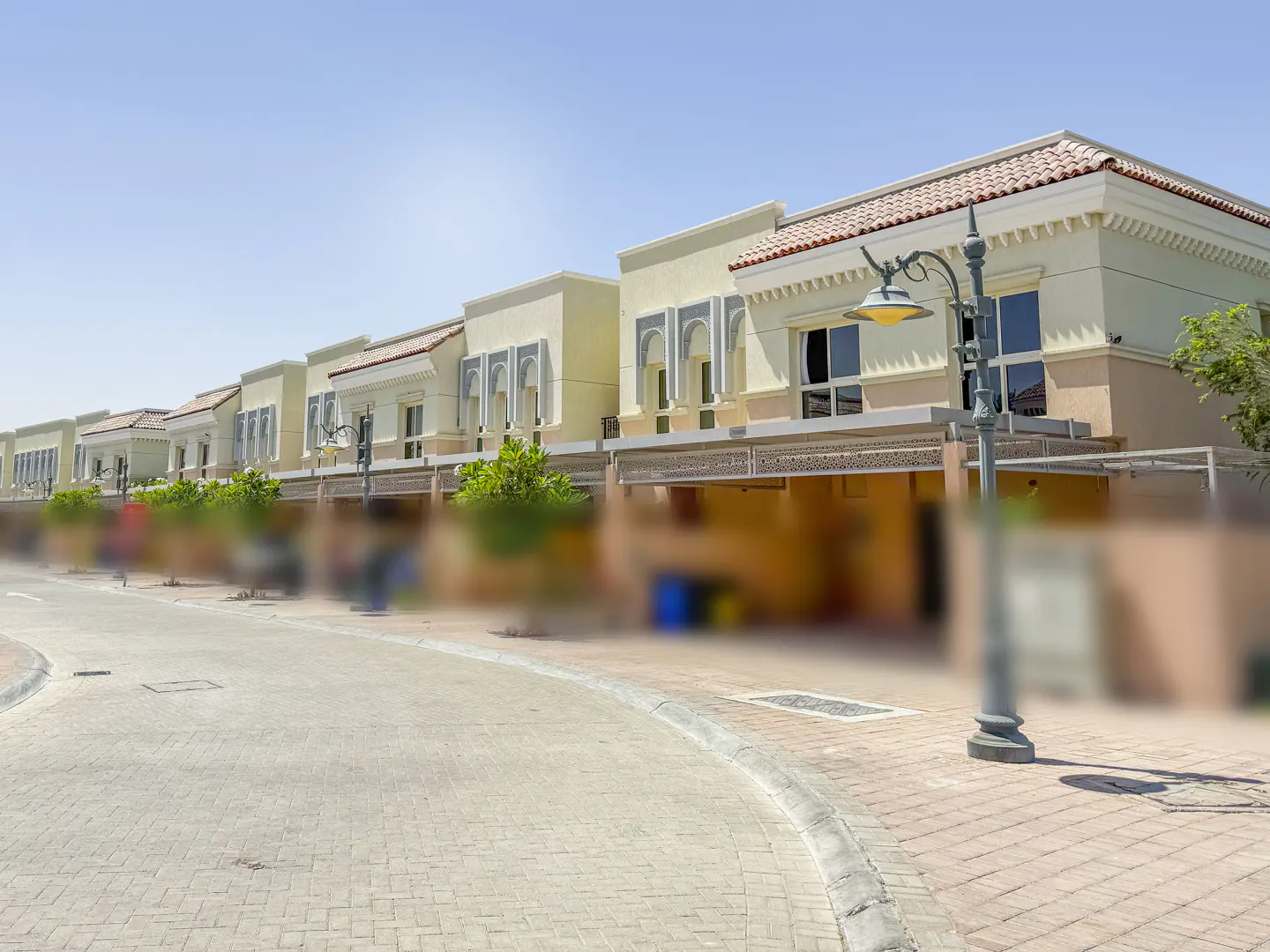 Row of light yellow townhouses with red tile roofs and arched windows, street lamp in foreground, blue sky.